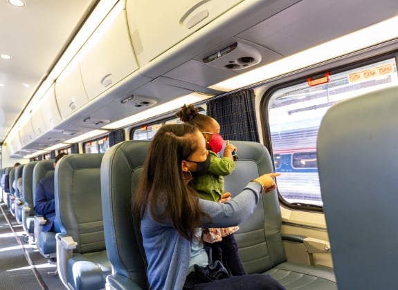 mother looking out the window and pointing with her daughter onboard amtrak in facial coverings