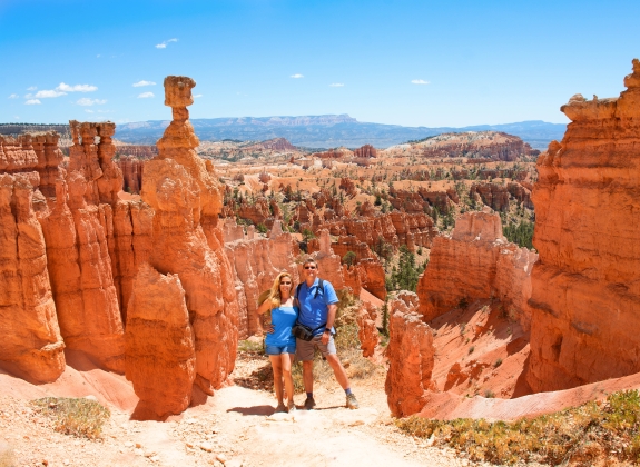 People enjoying summer hiking trip standing next to famous Thor's Hammer hoodoo. Smiling happy couple embracing on vacation in the red mountains. Bryce Canyon National Park, Utah, USA