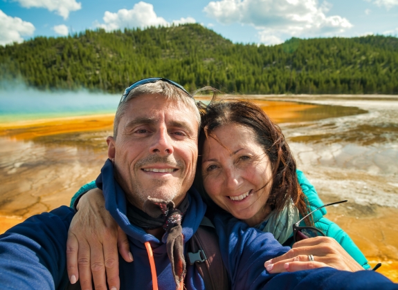 Happy couple making a selfie with the background of Grand Prismatic Spring Geyser, Yellowstone National Park.