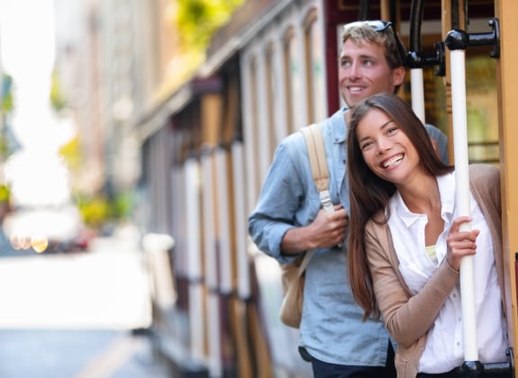San Francisco city tourists riding cable car tramway tourism people lifestyle. Young interracial couple enjoying ride of cable car railway system, popular travel attraction.