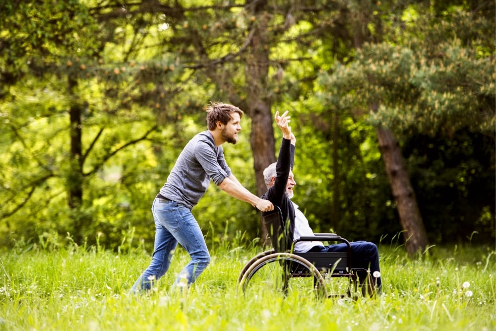 man pushing his father in a wheel chair through a field